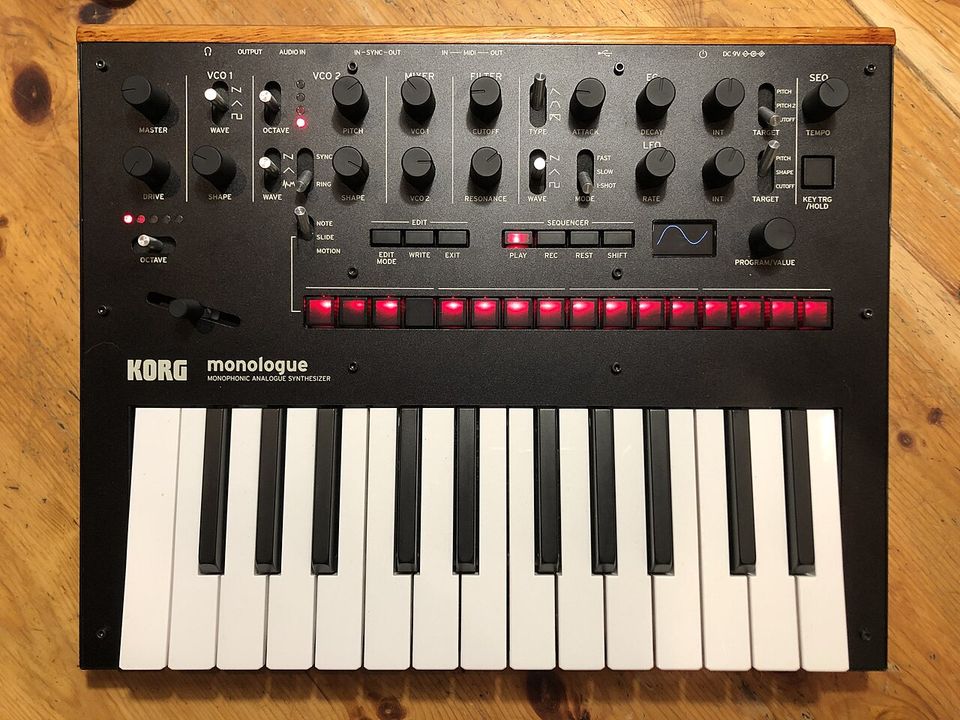 Top-down view of a Korg monologue with a wooden end cap, rows of knobs, sixteen red step buttons and a 25-key keyboard.