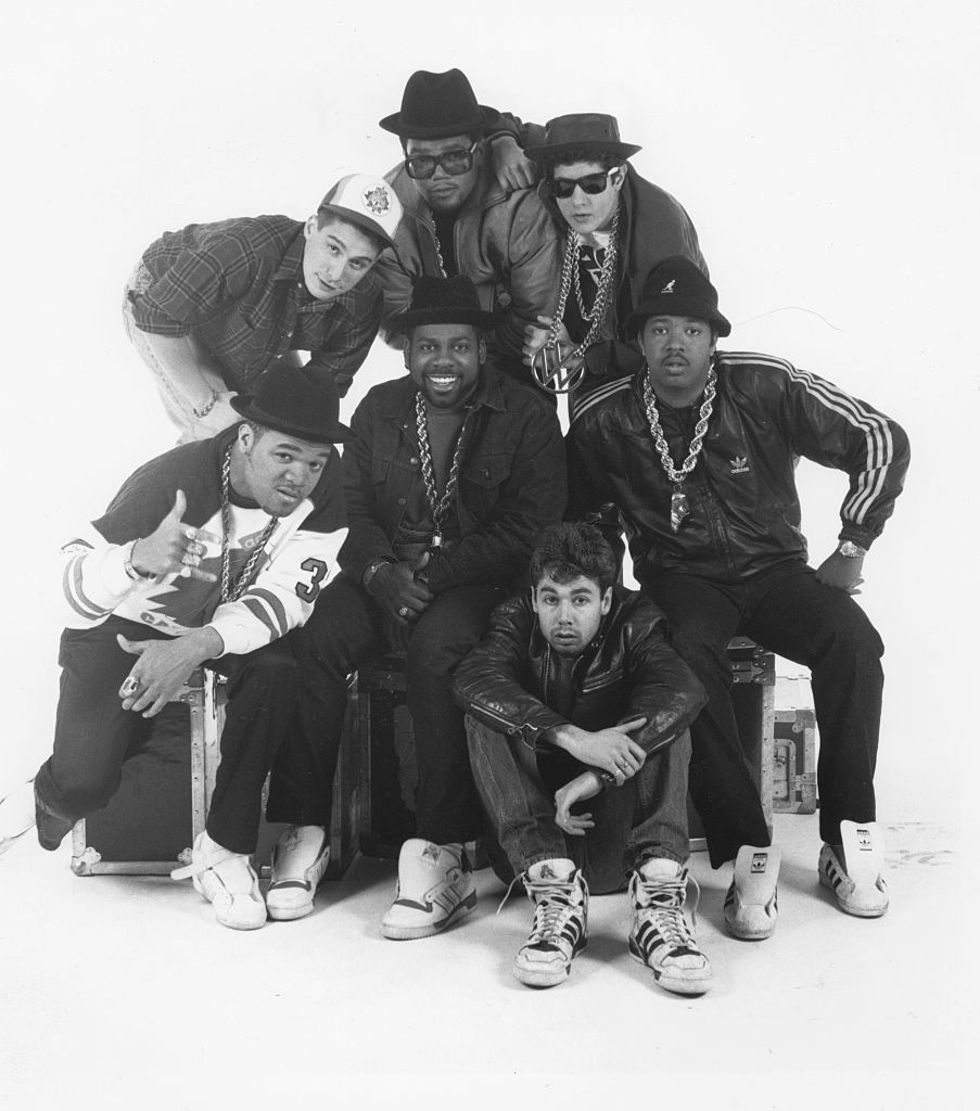 The Beastie Boys and Run-DMC posing together in a black and white studio photo, with DJ Hurricane at the bottom left